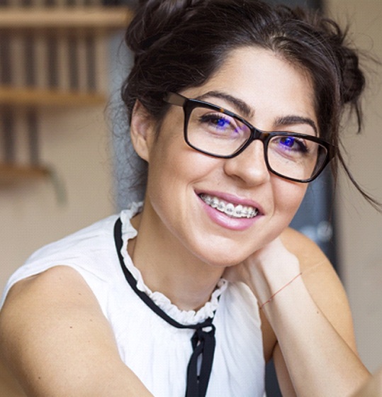 A young female wearing glasses and braces smiling while seated inside