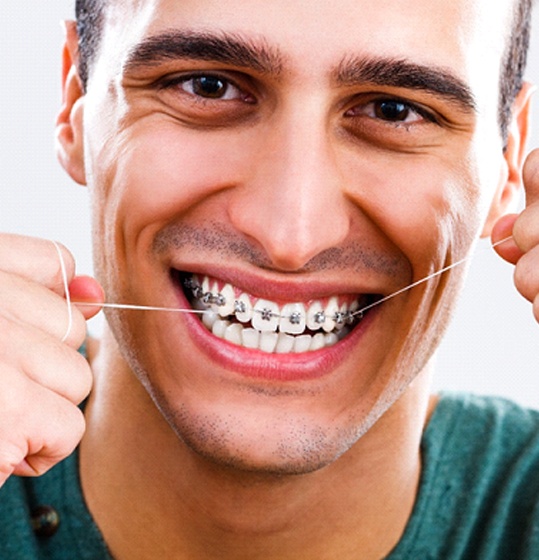 An older male teenager with braces on his top row of teeth attempting to floss