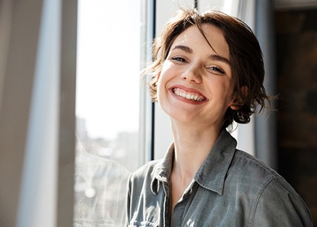 Young woman standing next to window and smiling