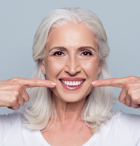 Woman pointing to smile after full mouth reconstruction