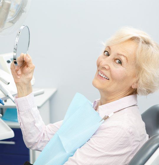 Woman looking at smile after dental bridge restoration