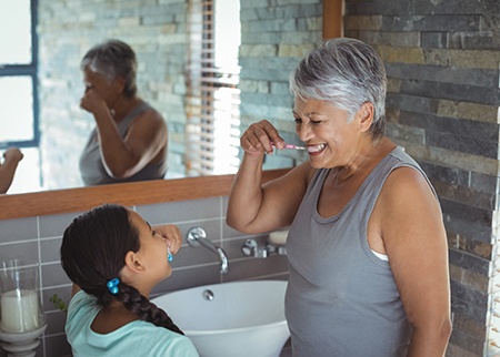 a person with dental implants in Denison brushing their teeth with their grandchild 