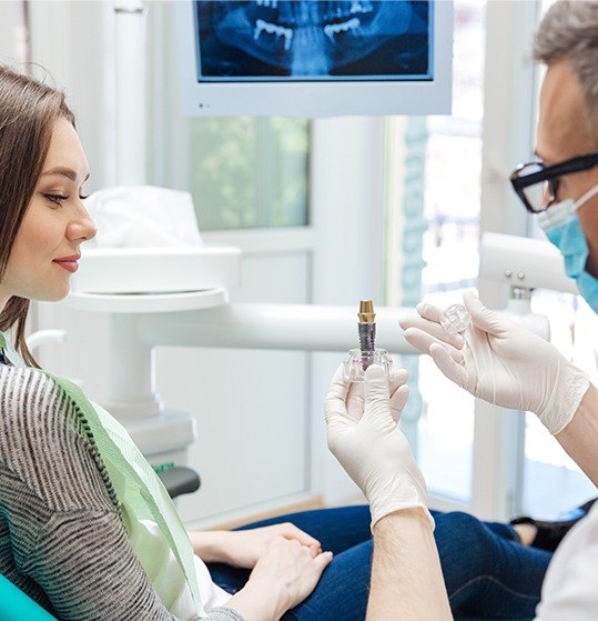 Dentist showing woman a dental implant post model