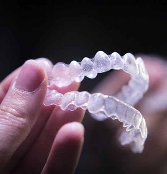 A person holding a pair of clear aligners.