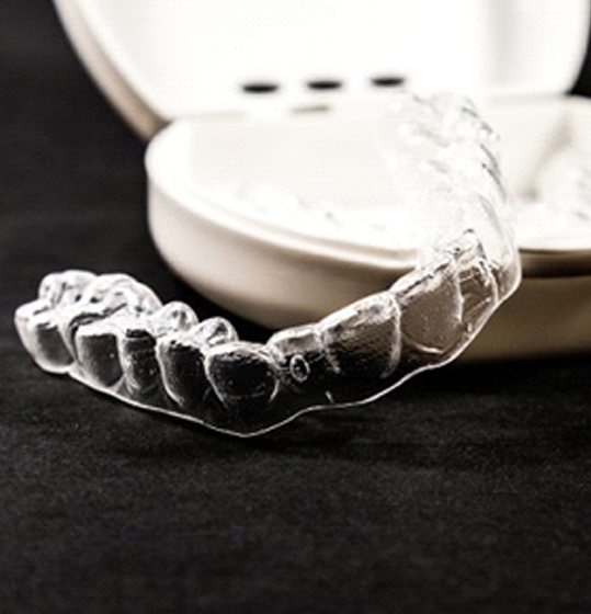 A clear aligner resting on a carrying case.