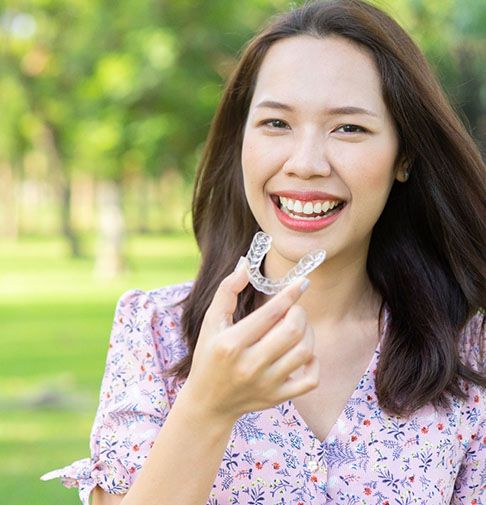 a patient smiling and holding their Invisalign aligner in Denison