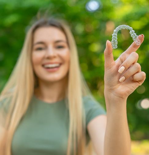 Teenage girl smiling while holding clear aligner