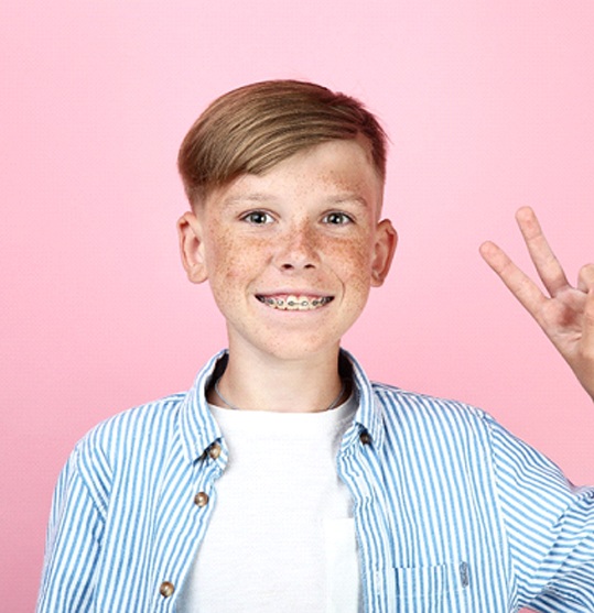 boy with traditional braces giving peace sign against pink background