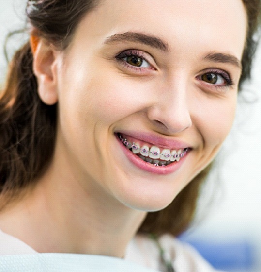 smiling female orthodontic patient with pink traditional braces
