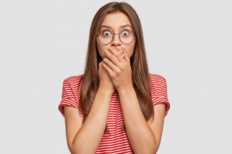 Closeup of woman in glasses covering her mouth in shock