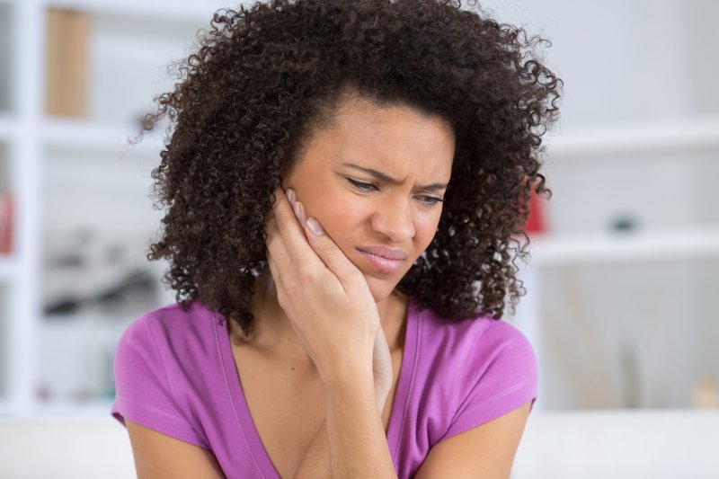 person with tooth pain holding their cheek