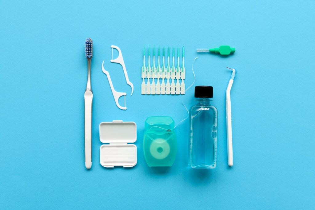 Various toothbrushes, floss, and ortho wax on blue surface